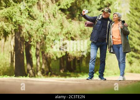 Full length portrait of active senior couple taking selfie photo via smartphone while enjoying hike in forest, copy space Stock Photo