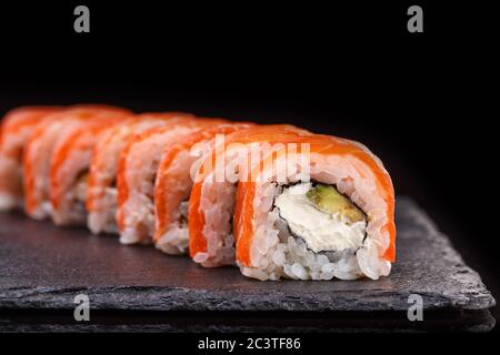 Philadelphia sushi rolls with salmon and cream cheese and avocado on a black slate plate close up.