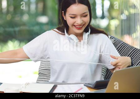 Asian woman student sitting at the table in living room, using computer laptop when studying online course Stock Photo