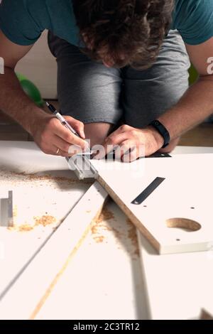 Man doing renovation work at home, drilling with a screwdriver. Group of repair tools on wooden white background.