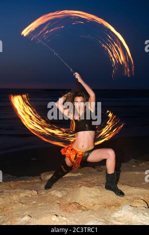 a female fire juggler juggles fire on the beach at sun set Stock Photo