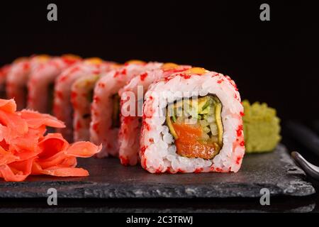 Roll with red caviar of fresh salmon, cream cheese, cucumber, avocado. Served with ginger and wasabi on black ceramic slate. Stock Photo