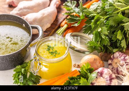 Chicken broth in a glass jar raw chicken legs carrot onion celery herbs garlic and fresh vegetables Stock Photo