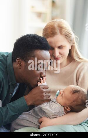 Vertical portrait of young interracial couple focus on African-American man kissing tiny hand of mixed-race baby Stock Photo