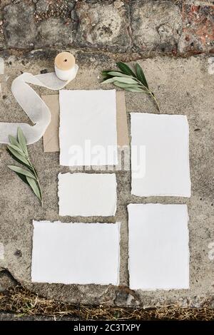 Summer wedding stationery mock-up scene. Blank greeting cards, envelopes, silk ribbon and olive branches on grunge concrete background.Vertical Stock Photo