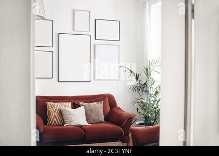 Blank picture frames mockups on white wall. White living room design. View of modern boho, scandi style interior with sofa, cushions, potted palm Stock Photo