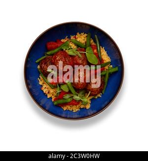 A delicious bowl of chipolte meat balls, couscous and vegetables, in a rustic blue bowl isolated on a white background Stock Photo