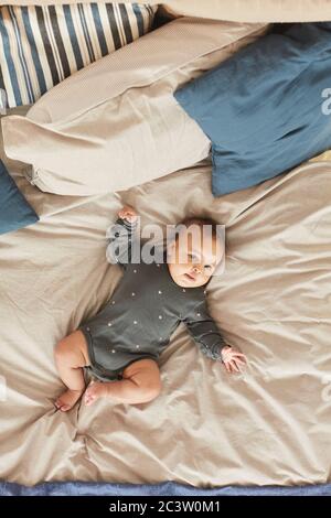 Vertical top down view at cute mixed-race baby lying on comfortable bed with fluffy blue and white blankets, copy space Stock Photo