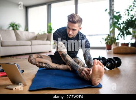 Front view portrait of man with tablet doing workout exercise indoors at home. Stock Photo