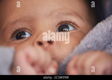 Close up portrait of cute mixed-race baby sucking thumb with focus on big hazel eyes with long lashes, copy space Stock Photo