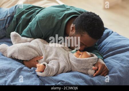 Portrait of loving African-American father kissing cute baby while lying on bed in cozy home interior, copy space Stock Photo