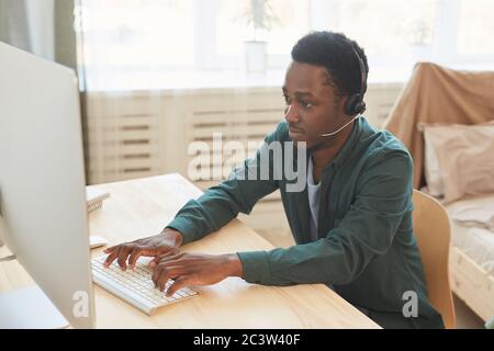 Portrait of young African-American man wearing headset and using computer while working from home, copy space Stock Photo