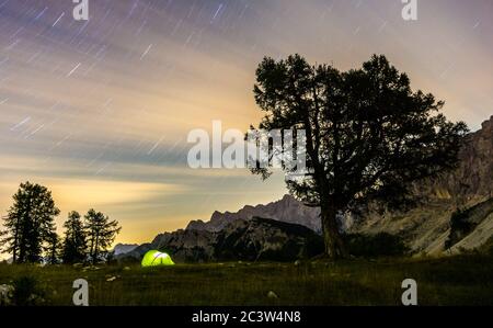 A tent glows under a star trails night sky at twilight hour. Julian Alps, Triglav National Park, Slovenia, Mountain Slemenova, Sleme. Stock Photo