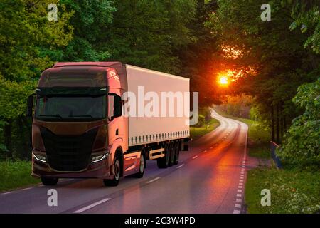 modern truck on the road leading through the forest at sunset Stock Photo