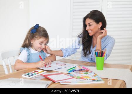 Smiling mother and daughter preparing for lessons and draws at the table with pencils and paints. Parent and pupil of preschool. First day of fall Stock Photo