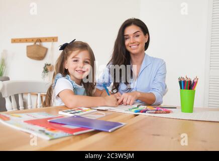 Smiling mother and daughter preparing for lessons and draws at the table with pencils and paints. Parent and pupil of preschool. First day of fall Stock Photo