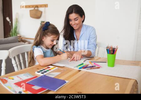 Smiling mother and daughter preparing for lessons and draws at the table with pencils and paints. Parent and pupil of preschool. First day of fall Stock Photo