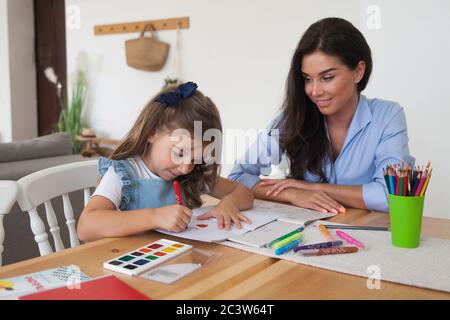 Smiling mother and daughter preparing for lessons and draws at the table with pencils and paints. Parent and pupil of preschool. First day of fall Stock Photo