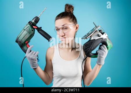 Drill and jigsaw in the hands of a girl in safety glasses Stock Photo