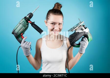 A cunningly smiling girl and power tools in her hands - a jigsaw and a drill Stock Photo