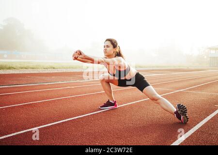 Athletic woman stretching on running track before training, healthy fitness lifesty