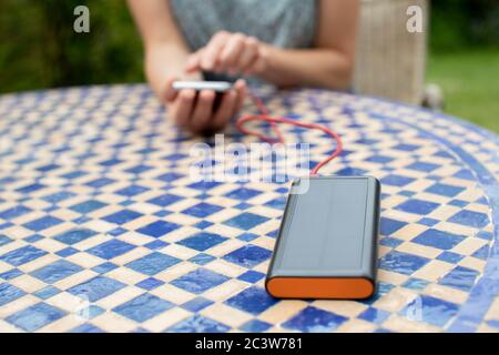 Woman Charging Mobile Phone Outdoors At Home With Portable Solar Power Bank Stock Photo