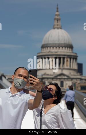 Millennium Bridge, London, England. 22nd June 2020. A couple, wearing protective face masks, pose for a selfie at Millennium Bridge over looking St Pauls Cathedral. Following the British governments relaxing of coronavirus lockdown laws a week ago today, lockdown life continues in central London, England. (photo by Sam Mellish / Alamy Live News) Stock Photo