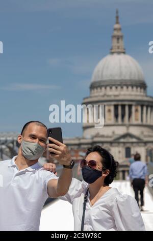Millennium Bridge, London, England. 22nd June 2020. A couple, wearing protective face masks, pose for a selfie at Millennium Bridge over looking St Pauls Cathedral. Following the British governments relaxing of coronavirus lockdown laws a week ago today, lockdown life continues in central London, England. (photo by Sam Mellish / Alamy Live News) Stock Photo