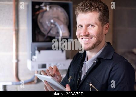 Portrait Of Male Heating Engineer Servicing Central Heating Boiler Using Digital Tablet Stock Photo