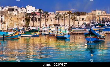 Marsaxlokk village and traditional boats reflected in the sea at sunset on the harbor of Malta Stock Photo