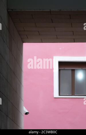 Composition of parallel and perpendicular lines with a window and a security camera on a magenta wall, framed with blocks of gray cement. Stock Photo