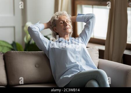 Relaxed 55s woman leaned on couch daydreaming in living room Stock Photo