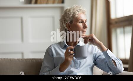 Mature woman drinks coffee looking in distance enjoy calm life Stock Photo