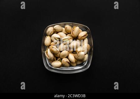 Pistachios in a small plate on a black table. Pistachio is a healthy vegetarian protein nutritious food. Natural nuts snacks. Stock Photo