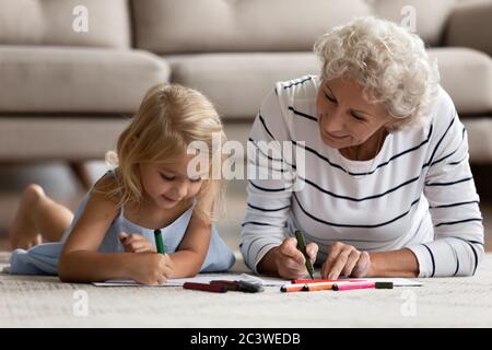 Old grandma little grandkid drawing pictures lying on warm floor Stock Photo