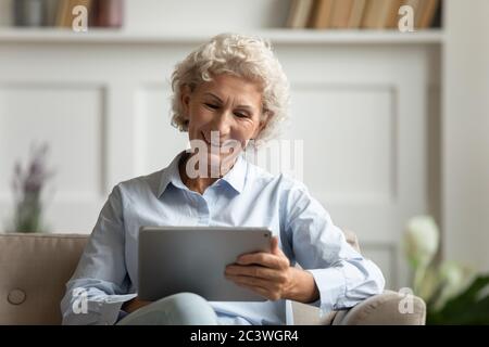 Aged woman using tablet websurfing chatting with friends using messenger Stock Photo