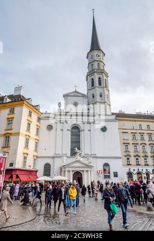 View of Saint Michael Church ( Michaelerkirche) one of the oldest churches in Vienna and the Michaelerplatz square filled with people, Vienna, Austria. Stock Photo