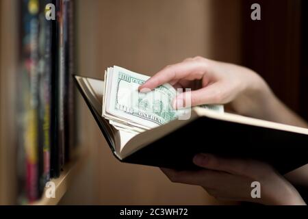 girl's hand puts or takes out savings in dollars from a paper book Stock Photo