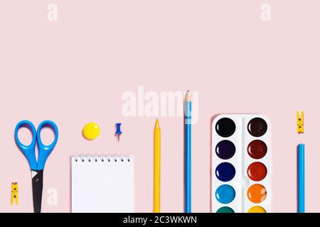Back to school flat lay with blue and yellow pencils, paper clips, cissors, watercolor and notepad on pink background. Stock Photo