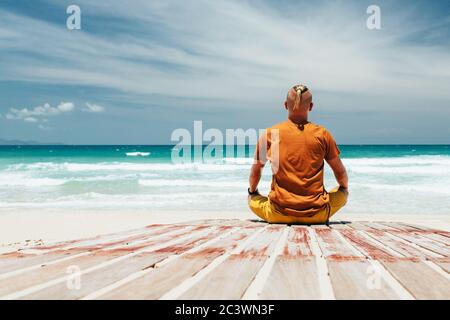 guy sits on the shore of a tropical beach The view from the back, the place of meditation, relaxation, during summer vacation. A panoramic view of the Stock Photo