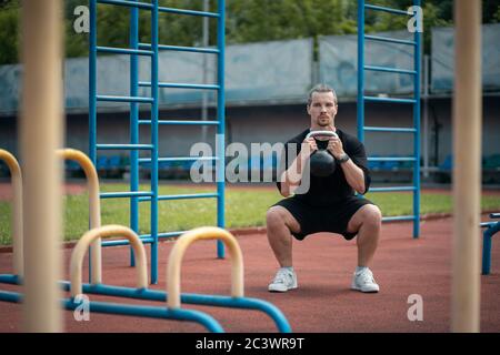 young athlete has workout and doing sport exercises with kettlebell outdoor Stock Photo