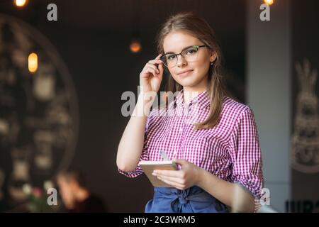 Portrait of a beautiful friendly waitress in glasses with notepapers and pen ready to take your order Stock Photo