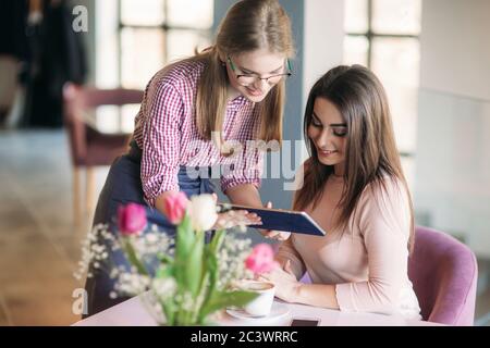 Attractive young waitress using a tablet computer to take an order from a customer in cafe. Beautiful woman look it tablet and smile Stock Photo