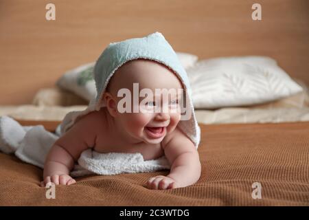 ute little baby lies on bed wrapped in white towel with hood Stock Photo