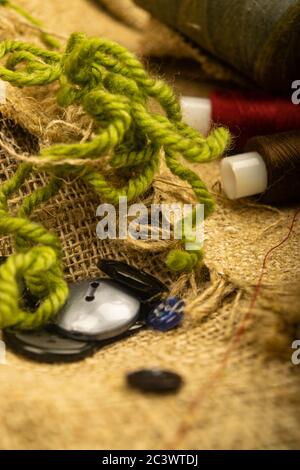 Various buttons and multicolored threads on coarse-textured burlap. Close up Stock Photo