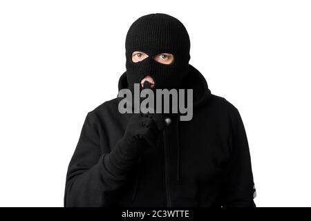 Thief in black balaclava holding fingers on lips Stock Photo