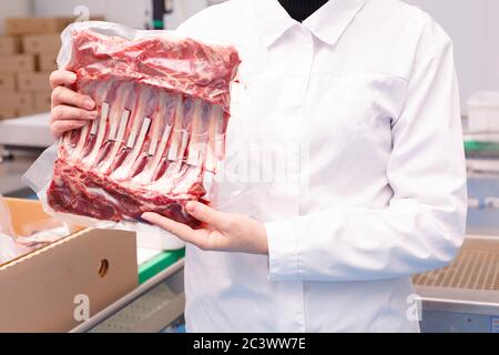 man with a white robe holds a semi-finished - lamb ribs with vacuum packaging Stock Photo