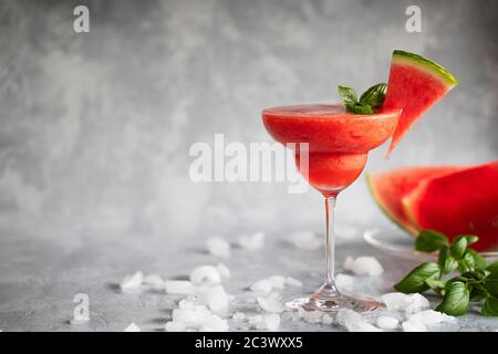 A fresh frozen blended margarita drink with strawberries and watermelon. The drink is garnished with basil leaves and watermelon. On ice scattered gra Stock Photo