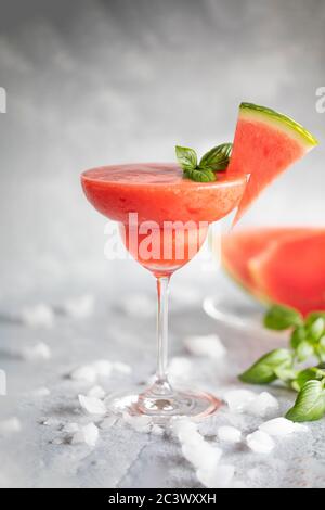 A fresh frozen blended margarita drink with strawberries and watermelon. The drink is garnished with basil leaves and watermelon. On ice scattered gra Stock Photo