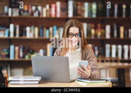 Young woman freelancer working on laptop and using cellphone Stock Photo